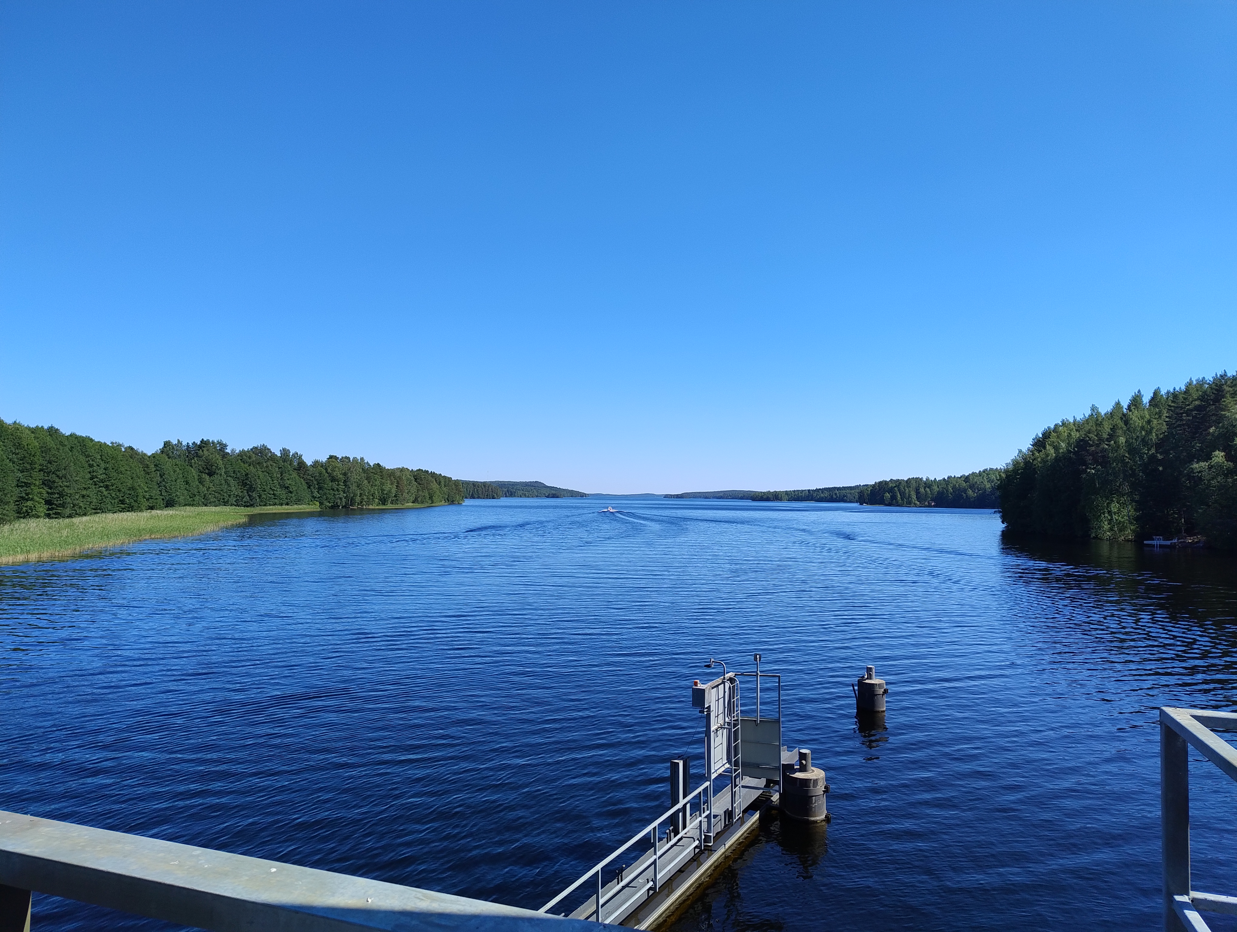 Päijänne kylpee auringossa, keskellä kuvaa valkoinen moottorivene