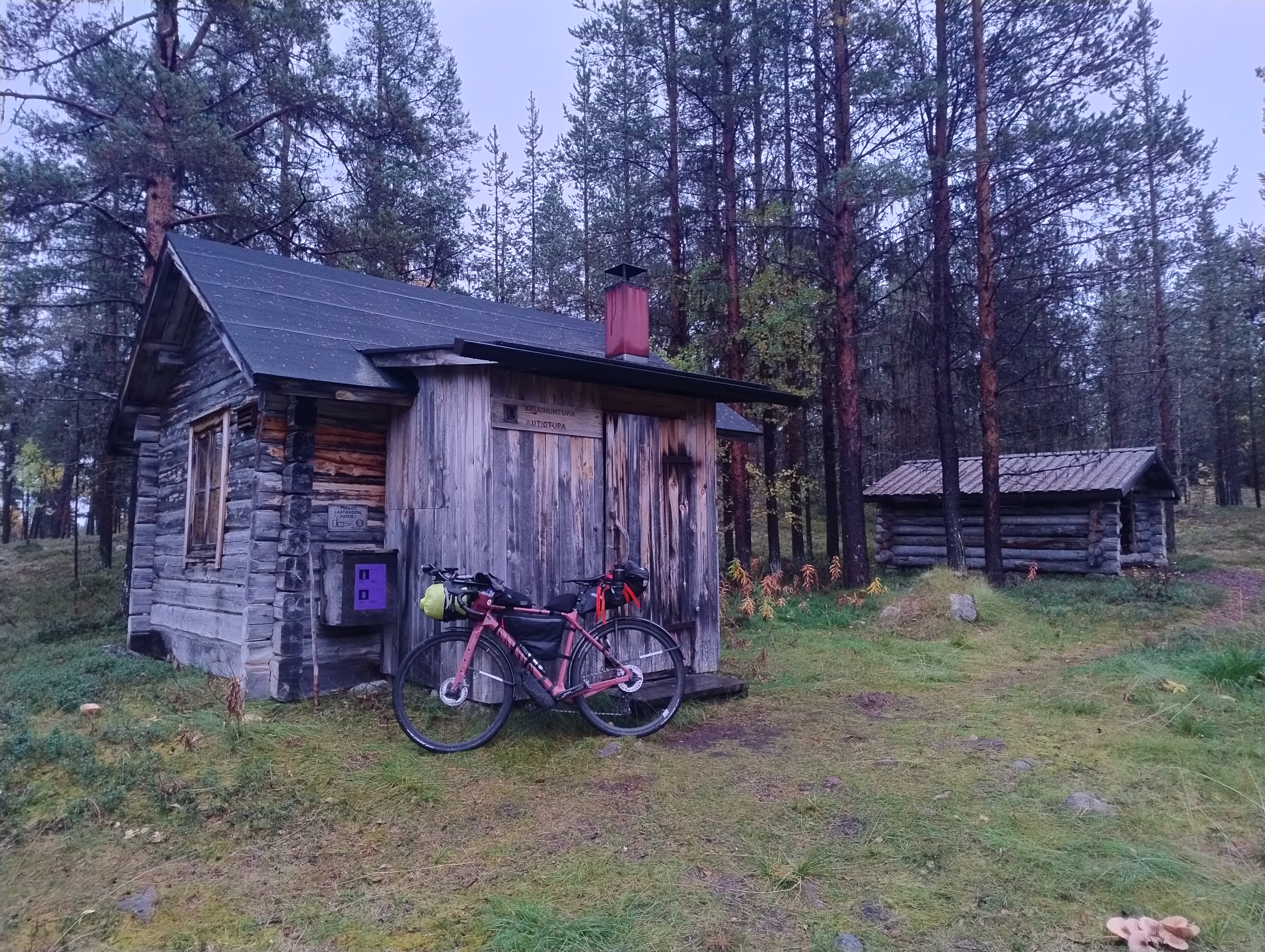Polkupyörä vanhan tuvan edustalla, taustalla puuliiteri