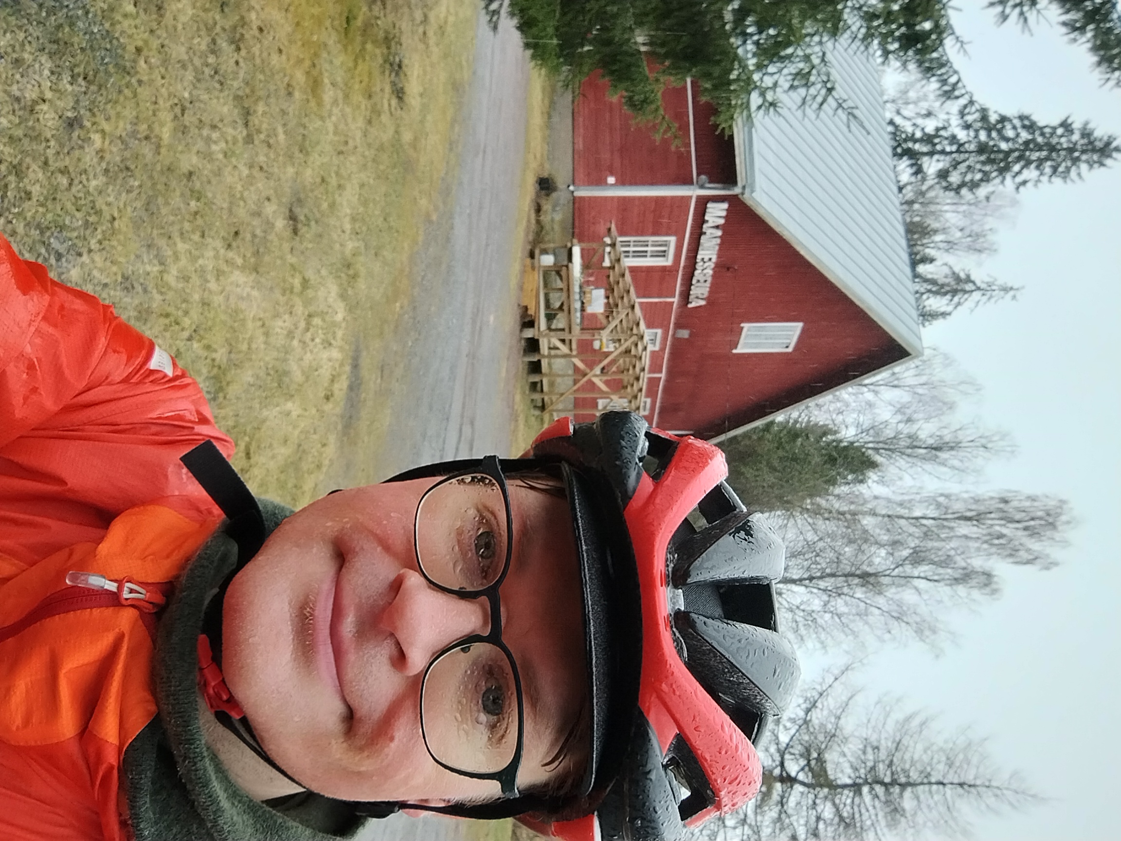 Olli sateesta märkänä punaisen talon edessä. Talon seinässä lukee Maamiesseura.